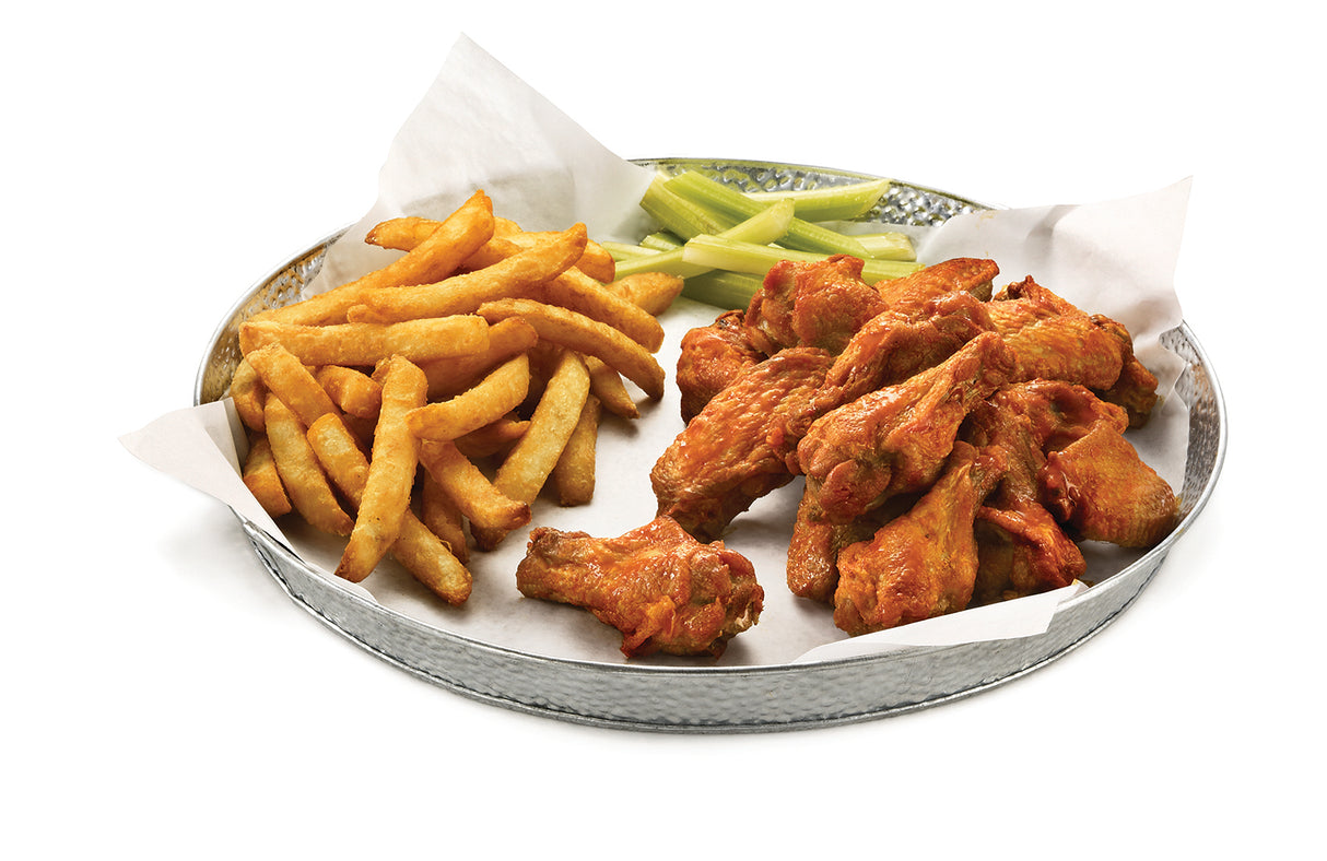 A round galvanized dinner platter by TableCraft, lined with parchment paper, holds golden French fries, buffalo chicken wings coated in sauce, and a few celery sticks—all neatly arranged on a white background.
