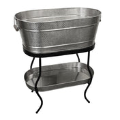 A large, oval-shaped, silver metal beverage tub with a hammered texture sits on a black TableCraft Products beverage tub stand. The stand features curved legs and supports a matching smaller tray below. The tub has a handle on one side.