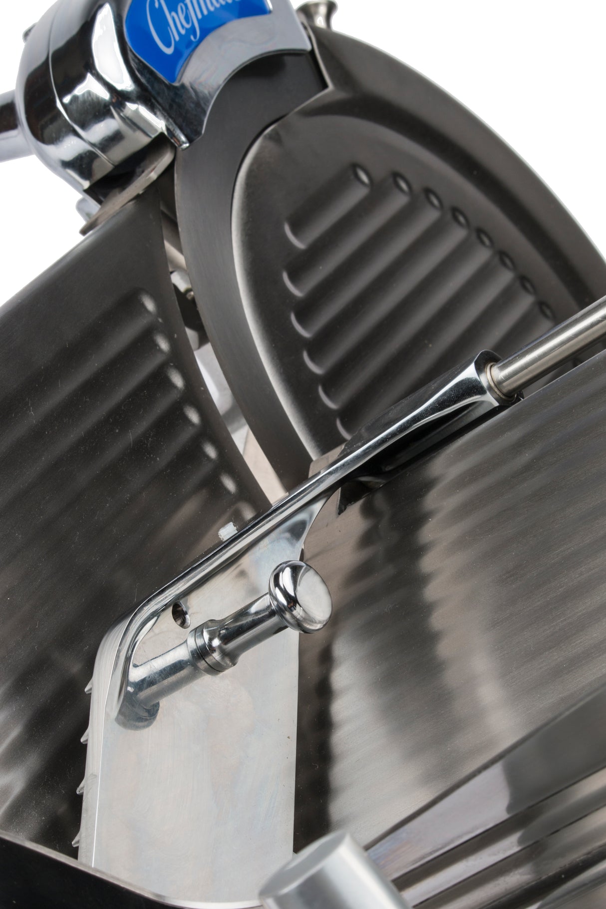 Close-up of a compact slicer from the Chefmate Series, featuring a circular serrated blade and adjustable thickness lever. Grooved surface and stainless steel construction shine under light. A blue label with partial text appears at the top.