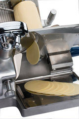 A cylindrical block of cheese is being sliced by a compact Chefmate Series deli slicer. Thin, oval slices fall onto a metal tray below the blade. The shiny 12 inch slicer is shown against a white background.