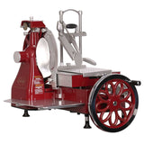 A vintage-style Italian-designed flywheel slicer with a large hand-crank wheel, shiny metal blade, and polished parts. The flat platform holds food, while adjustment knobs and decorative spokes with chrome trim complete the classic look.