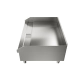 A stainless steel industrial sink or workstation with raised back and side edges, a rectangular cutout on the left side, and four short legs, photographed beside an electric countertop griddle against a white background.