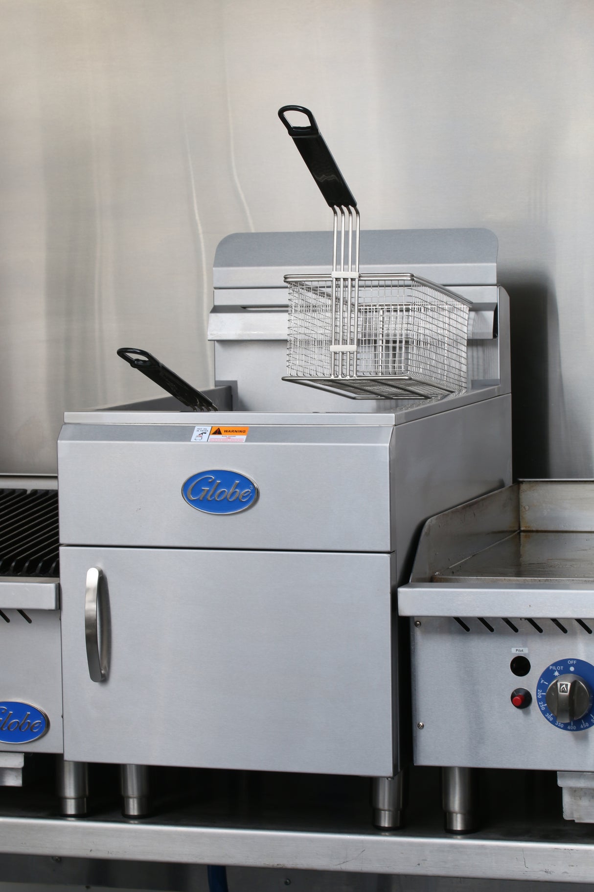 A commercial 30-lbs fat capacity stainless steel fryer with a rectangular frying basket and black handle. The blue Globe logo is displayed on the front, and this gas countertop fryer sits among other kitchen appliances.