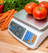 Three tomatoes rest on a price computing scale, its dual LCD display showing their weight and price. Surrounded by carrots, lettuce, and a red bell pepper on wood, the legal for trade scale’s keypad and screen detail every measurement.
