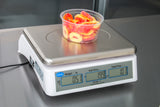 A clear plastic container filled with red and yellow candy rings sits on a price computing scale with a dual LCD display. The scale, legal for trade, shows a weight of 0.51 lb, unit price of 1.99, and total price of 1.01 on the stainless steel countertop.