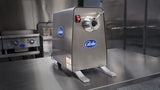 A stainless steel Globe brand meat grinder with 1 HP Power Drive Unit is on a reflective metal countertop in a commercial kitchen, with appliances and cabinets in the background. The grinder has a round feed tube, on/off switch, and stands on two sturdy legs.