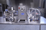 A stainless steel commercial meat grinder with 1 HP Power Drive Unit and food processor sit on a metal counter in an industrial kitchen. Both machines feature “Globe” logos, large attachments, and durable stainless steel construction.