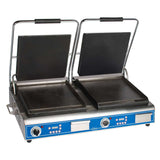 A double countertop electric grill and sandwich panini grill with two open, flat black cast iron smooth plates. Each side has a handle and control knobs with indicator lights on a blue front panel. Stainless steel body stands on four short legs.