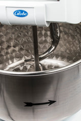 Close-up of a commercial spiral dough mixer with a Globe label, featuring a spiral dough hook inside a large, textured stainless steel bowl. A black arrow sticker on the bowl indicates its rotational direction; this model boasts 130 lbs capacity.