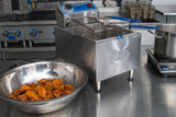 A commercial kitchen with a Globe PF16E electric countertop fryer, 16 lbs. oil capacity, stainless steel basket inside, and a bowl of cooked chicken wings on the metal counter. Stovetop, grill, and fryer baskets are organized on clean surfaces in the background.