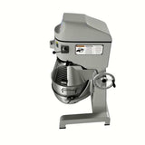 A commercial mixer with a large metal mixing bowl, protective wire guard, and side-mounted hand crank. This 60 qt mixer features a gray body, visible warning labels, and is designed for heavy-duty food preparation in professional kitchens.