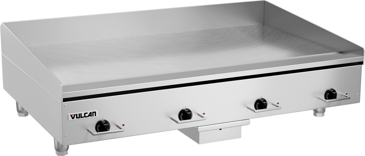 A large heavy duty griddle with four black control knobs on the front, labeled Vulcan. The flat polished steel griddle plate has raised back and sides. Four short legs support the unit, with a small drawer beneath the center.