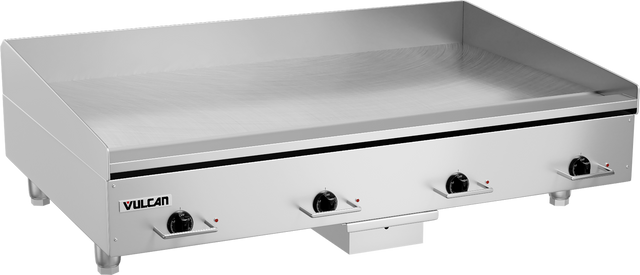 A large heavy duty griddle with four black control knobs on the front, labeled Vulcan. The flat polished steel griddle plate has raised back and sides. Four short legs support the unit, with a small drawer beneath the center.