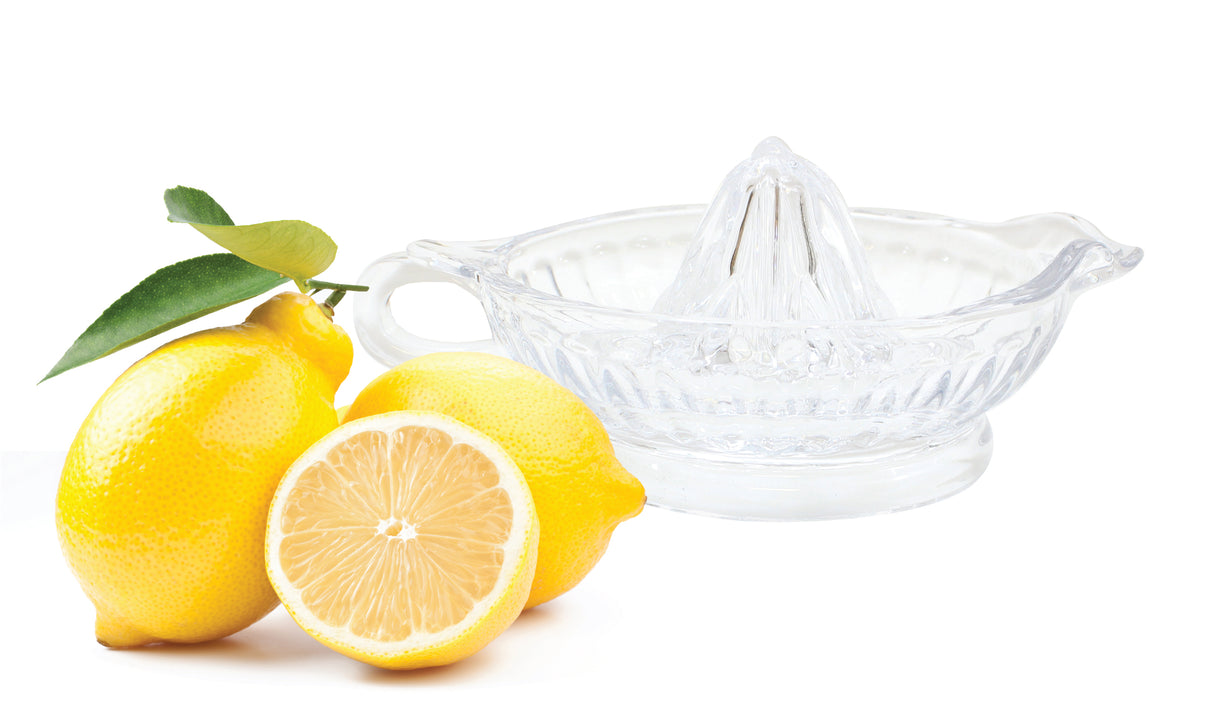 Two whole lemons, one with leaves, and a halved lemon sit next to a clear TableCraft glass juicer. The white background highlights the bright yellow lemons and the transparent juicer beautifully.