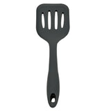 A black Cash & Carry Turner slotted spatula with a wide, flat, heat resistant silicone head featuring four rectangular slots. The solid, slightly curved handle has a hole at the end for hanging.