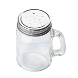 A small, clear glass jar salt shaker with a handle and a silver metal lid featuring multiple holes, resembling a Mason salt/pepper shaker, is shown isolated on a white background.