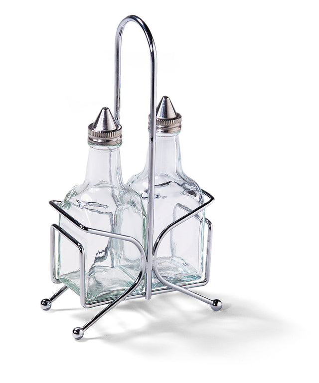 Two clear glass bottles with metal spouts sit in a silver metal stand. Perfect as an Oil & Vinegar Dispenser Set from TableCraft, the stand features four ball feet and a tall handle, keeping the square-shaped bottles upright on any Cash & Carry display.
