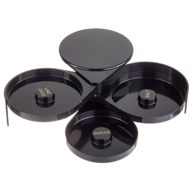 A sleek, glossy TableCraft glass rimmer featuring three circular trays labeled LIME JUICE, SALT, and SUGAR in gold text. The black, tiered design fans out for easy cocktail prep and is conveniently dishwasher safe.