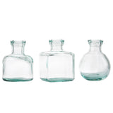 Three clear recycled glass bottles with short necks and wide mouths stand side by side. These versatile vases—cylindrical, square, and round—are empty, transparent, and set against a plain white background.