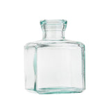 A small, clear recycled glass bottle with a short neck and a wide, flat, square-shaped body. The empty vase features a smooth surface with slightly rounded edges and is photographed on a white background.
