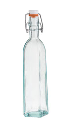 A clear, empty TableCraft glass bottle with a square base and rounded shoulders, crafted from recycled glass and topped with a white ceramic swing-top lid and metal clasp. This resealable bottle stands upright against a plain white background.