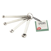 A set of four stainless steel measuring spoons labeled smidgen, pinch, dash, and tad, attached to a metal ring. Complements J.A. Henckels Steel tools perfectly. A green and white tag reads “Spoons, Stainless Steel, set of 4, For Craft Kitchen.”.