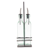Two green tint glass bottles with stainless steel pourers stand side by side in a black metal holder. The holder features a central handle and a rectangular base with horizontal bars to keep the bottles upright and secure.