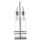 Two clear glass bottles with stainless steel pourers sit side by side in a sturdy metal rack. The rack features a central handle and square base, holding the simple, rectangular bottles upright and ready for use.