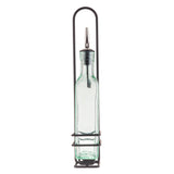 A clear glass oil bottle with a stainless steel pourer sits in a tall, black metal rack with a handle. The holder has three horizontal rings securing the bottle and an arched top for easy carrying. The empty glass bottle stands against a white background.