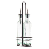 Two green tint glass bottles with stainless steel pourers are held upright in a black metal rack with a tall handle. The bottles are empty, and the rack encases them at the base and midsection for easy carrying and storage.