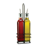 Two green tint glass bottles, one filled with red liquid (likely vinegar) and the other with yellow (likely olive oil), feature stainless steel pourers and sit side by side in a black metal holder from TableCraft Products, against a white background.