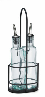 Two clear Gemelli bottle set glass oil and vinegar bottles with stainless steel pourers sit side by side in a black metal holder with a round base, vertical bars, and handle. The background is white.