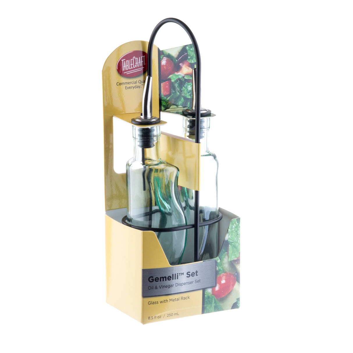 Two green tint glass bottles with stainless steel pourers are held in a black metal rack. The Gemelli bottle set comes packaged in a yellow TableCraft box with food images and is labeled as an Oil & Vinegar Dispenser Set, 8.5 fl oz / 250 ml.