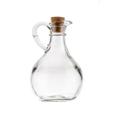 A clear glass bottle cruet with a rounded body, small spout, curved handle, and cork stopper. This Olive Oil Bottle by TableCraft Products is photographed against a plain white background.