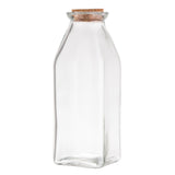 A clear Glass Milk Jar with a square base and rounded shoulders is topped with a light brown cork stopper. This TableCraft-style bottle stands upright against a plain white background, perfect for stylish storage or display.