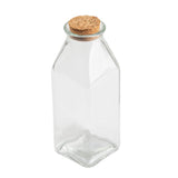 A clear, empty Glass Milk Jar with a square base and gently sloping shoulders, sealed with a round, light-brown cork stopper. Shown against a plain white background, the jar highlights its transparency and simple design.