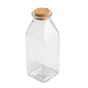 A clear, empty Glass Milk Jar with a square base and gently sloping shoulders, sealed with a round, light-brown cork stopper. Shown against a plain white background, the jar highlights its transparency and simple design.