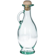 A clear olive oil bottle with a curved body, a small handle on one side, a narrow neck, and a round cork stopper at the top. The empty bottle stands upright on a white background.