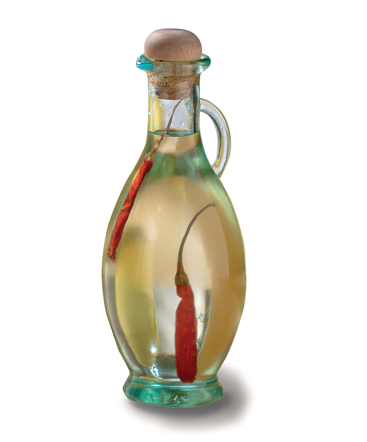 A clear olive oil bottle with a handle and cork stopper, filled with light yellow oil. Inside the bottle are two whole red chili peppers, partially submerged in the oil. The background is plain white.