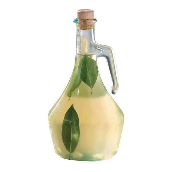 A TableCraft Olive Oil Bottle made of clear glass with a subtle green tint, featuring a side handle and cork stopper. Two bay leaves float in the pale yellow liquid inside. The background is plain white.