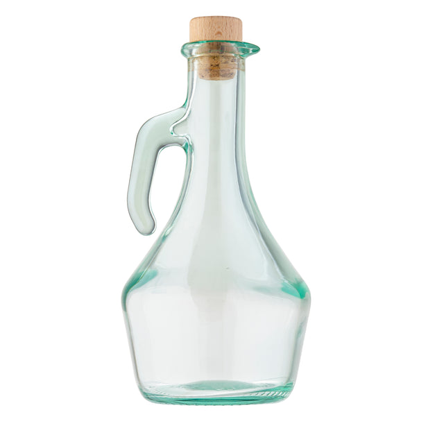 A clear TableCraft olive oil bottle with a wide base, narrow neck, and curved handle on one side. The empty bottle features a subtle green tint glass and is sealed with a round cork stopper. The background is plain white.