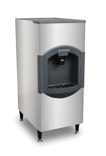 A stainless steel floor model ice dispenser with four black legs, a large front dispensing area, gray trim, and a visible "PUSH" button under the “Scotsman” brand above the chute. This hotel ice dispenser features a modern, angular design.