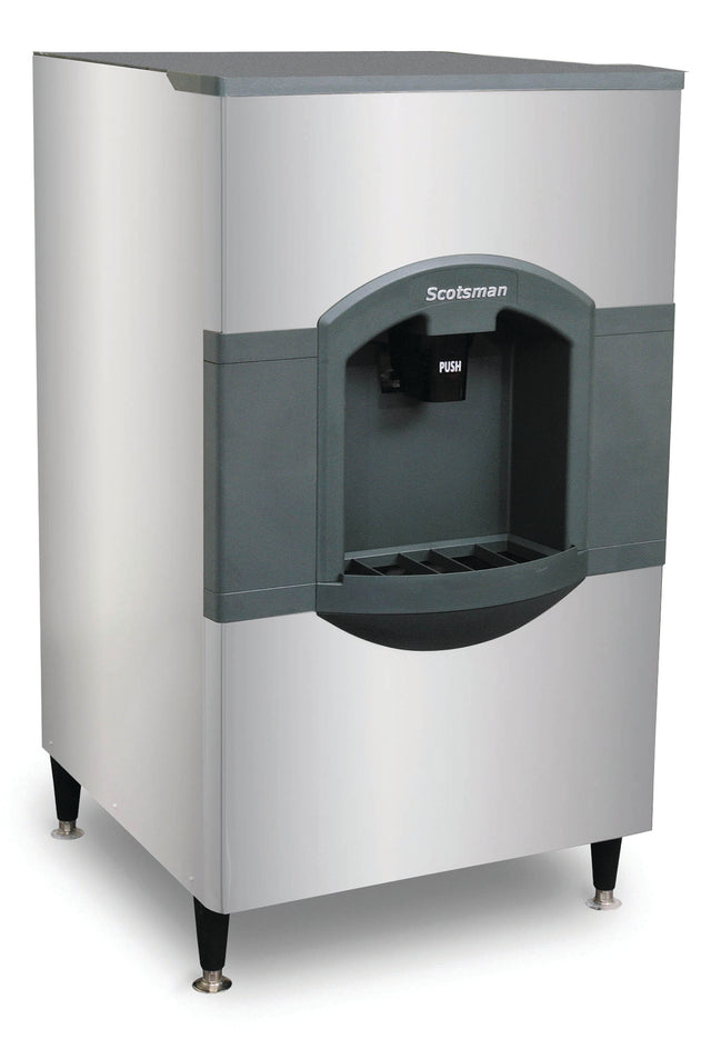 A large, stainless steel hotel ice dispenser with a gray front panel and 180 lb storage. The Scotsman name is above the dispensing area, which has a black PUSH lever and grated tray below to catch ice. The machine stands on four short legs.
