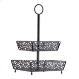 A two-tiered, black metal fruit basket with ornate, cut-out patterns on each tier. The rectangular trays are supported by a central pole and topped with a circular handle for easy carrying. Four small legs elevate the lower tier.