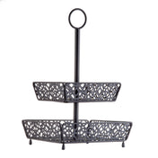 A two-tiered, black metal fruit basket with ornate, cut-out patterns on each tier. The rectangular trays are supported by a central pole and topped with a circular handle for easy carrying. Four small legs elevate the lower tier.