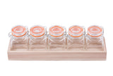 Five empty glass jars with orange rubber seals and metal clasps sit in a rectangular wood crate, arranged in a row like a tasting flight set against a white background.