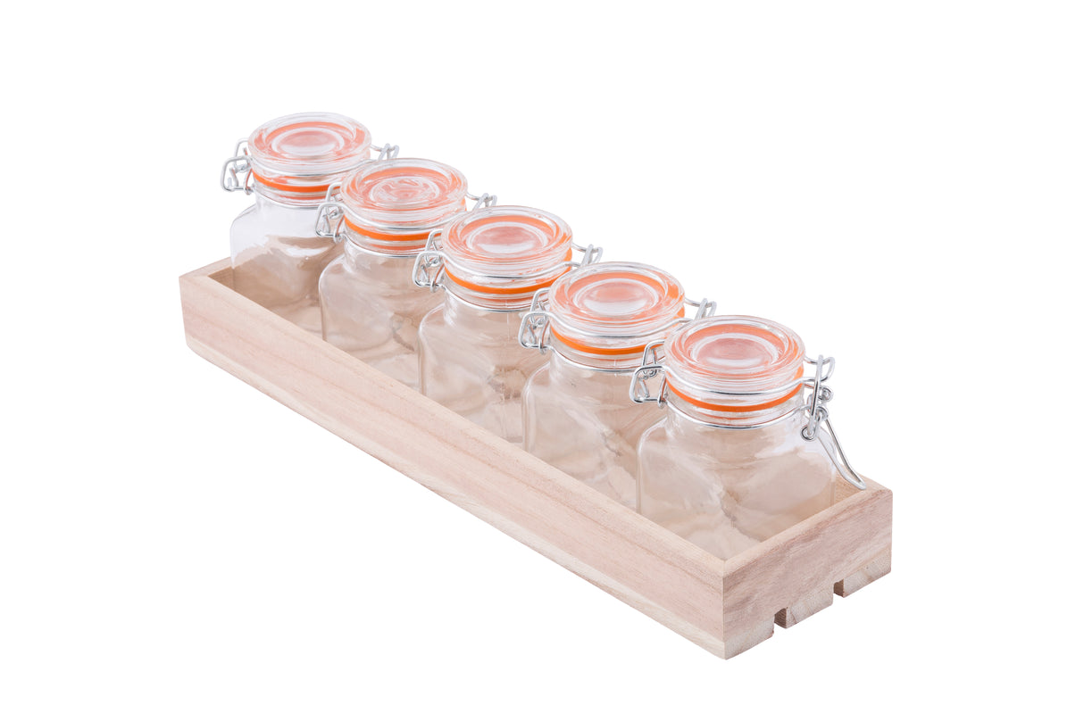 Five small, empty glass jars with orange-sealed clamp lids are arranged in a row inside a light wooden crate, perfect as a tasting flight set. The clear, identical jars are displayed against a white background.