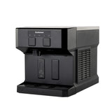 A black Scotsman compact ice and water dispenser with a boxy design, front control panel with buttons and indicator lights, two dispensing nozzles, and a drip tray at the bottom. The side features a vented panel. The background is plain white.