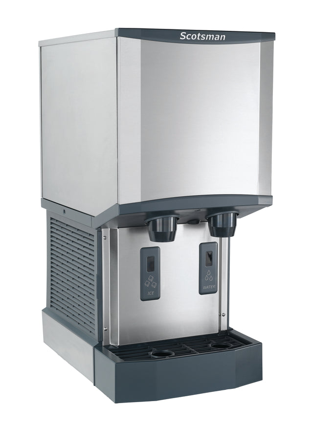A stainless steel Scotsman nugget ice machine and water dispenser with two push-button dispensers labeled Ice and Water, a drip tray beneath, and a modern, boxy design. The machine features a vented side panel and brand logo at the top front.