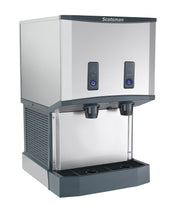 A stainless steel Meridian HID525WB-1 nugget ice machine and water dispenser with two black push buttons for ice and water, two spouts, a drip tray below, vented side panels, and a modern, boxy design set against a white background.